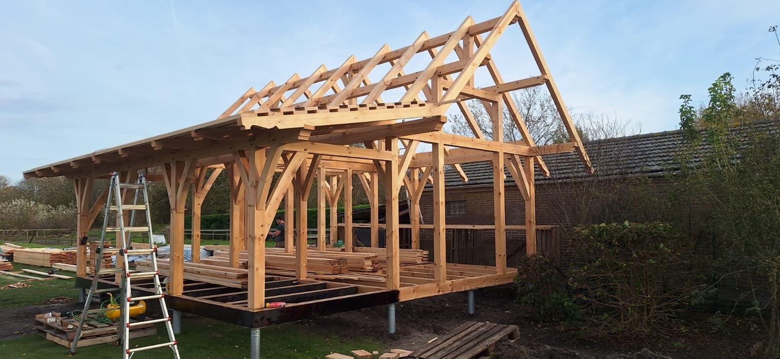 Timber frame annex being raised, rafters up, frame standing on screw piles